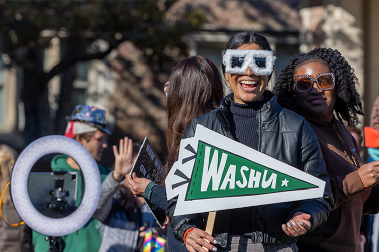 students smiling on campus holding WashU sign and wearing fun sunglasses