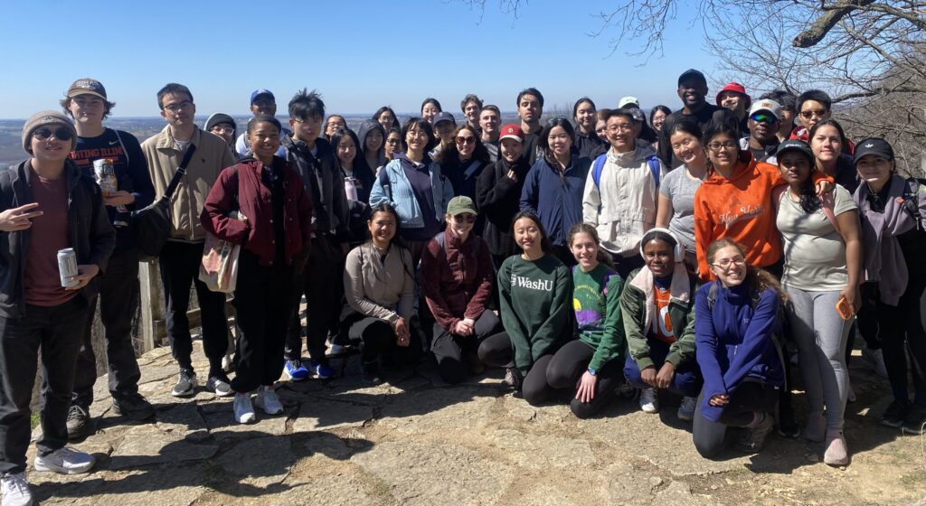 A large group of students in WashU gear pose for a photo on a hiking trail
